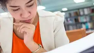 Moça pensando e lendo em biblioteca