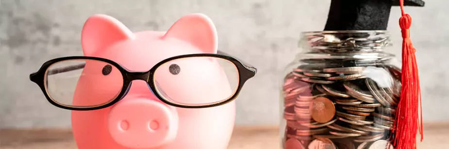 Cofrinho de porco com óculos ao lado de vidro de moedas, com chapéu de formatura em cima da tampa