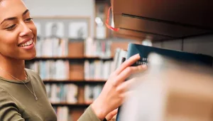 Moça escolhendo livro em biblioteca