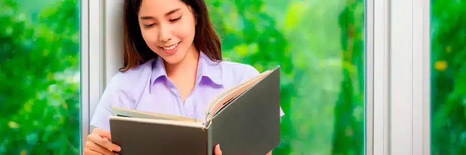 moça lendo livro contra janela
