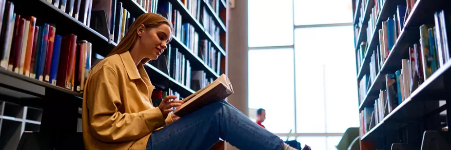 moça lendo livro sentada em chão de biblioteca